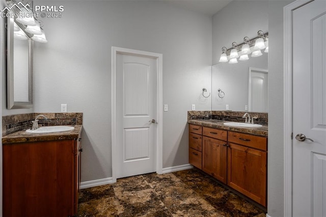 bathroom with stone finish floor, two vanities, a sink, and baseboards