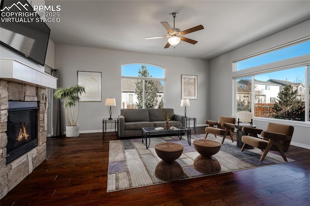 living room featuring ceiling fan, a stone fireplace, baseboards, and hardwood / wood-style flooring