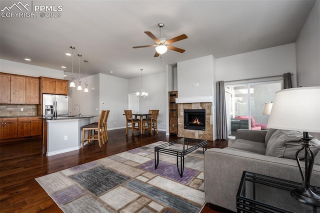 living area featuring a fireplace, recessed lighting, dark wood-type flooring, baseboards, and ceiling fan with notable chandelier