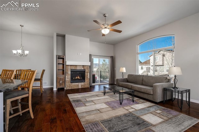 living room featuring a fireplace, baseboards, wood finished floors, and ceiling fan with notable chandelier