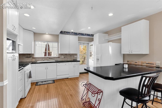 kitchen with white appliances, dark countertops, a breakfast bar area, a peninsula, and light wood-style floors