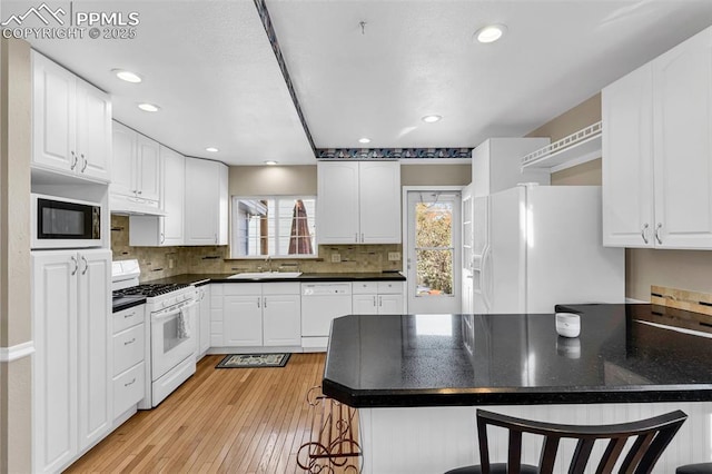 kitchen featuring a peninsula, white appliances, dark countertops, and a sink