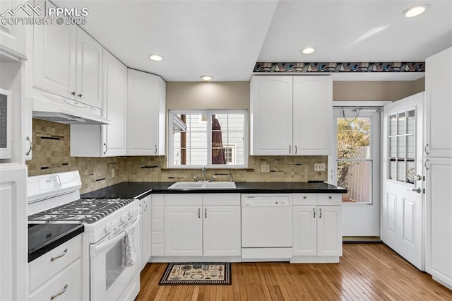 kitchen featuring dark countertops, white appliances, white cabinets, and a sink