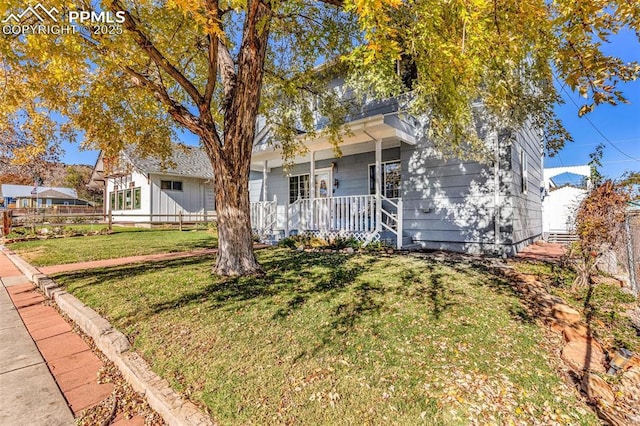 view of property hidden behind natural elements with a porch, a front yard, and a balcony