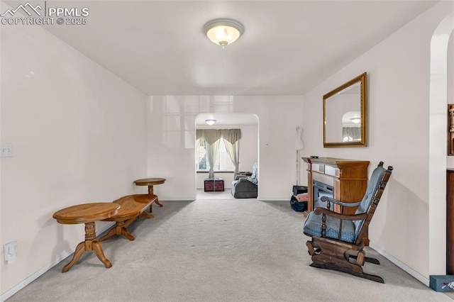 sitting room featuring carpet floors, arched walkways, a glass covered fireplace, and baseboards