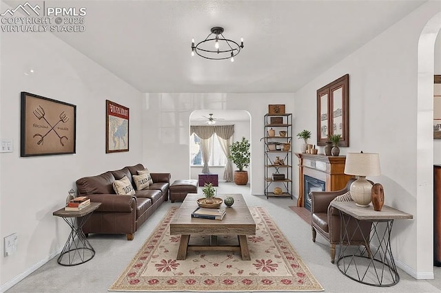 living area featuring arched walkways, baseboards, light colored carpet, a fireplace with flush hearth, and ceiling fan with notable chandelier