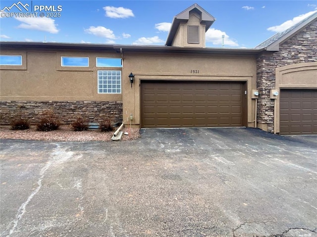 view of front of house with a garage, stone siding, aphalt driveway, and stucco siding