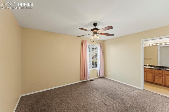 unfurnished bedroom with baseboards, a ceiling fan, light colored carpet, ensuite bath, and a sink