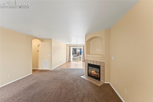 unfurnished living room with carpet, a fireplace, visible vents, and baseboards