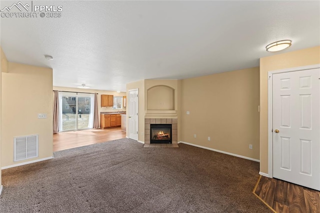 unfurnished living room with carpet floors, a tile fireplace, visible vents, and baseboards