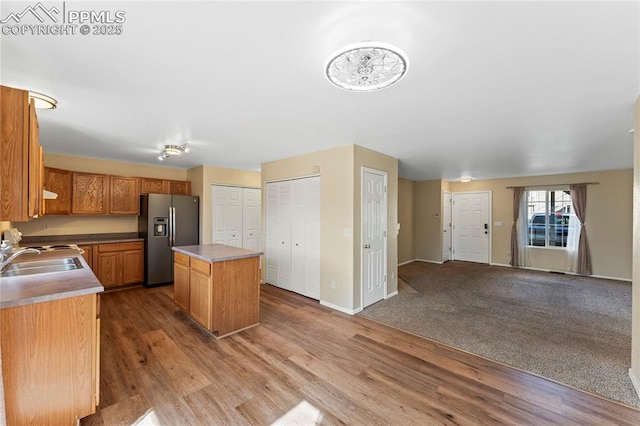 kitchen featuring open floor plan, a kitchen island, a sink, wood finished floors, and stainless steel fridge with ice dispenser