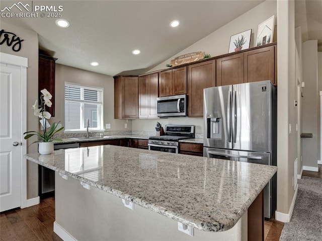 kitchen featuring light stone counters, a center island, lofted ceiling, appliances with stainless steel finishes, and a sink