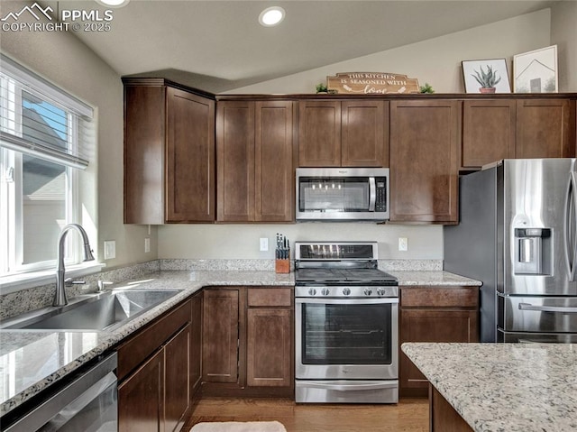 kitchen featuring lofted ceiling, light stone counters, recessed lighting, stainless steel appliances, and a sink