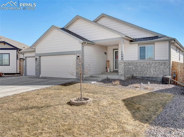 view of front of house featuring a garage, stone siding, fence, and driveway