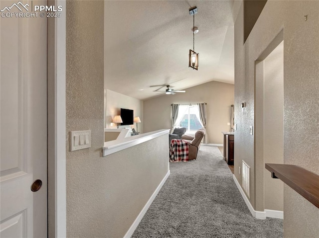 hallway with vaulted ceiling, a textured wall, carpet flooring, and baseboards