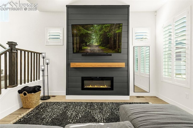 living room with a wealth of natural light, a large fireplace, baseboards, and wood finished floors