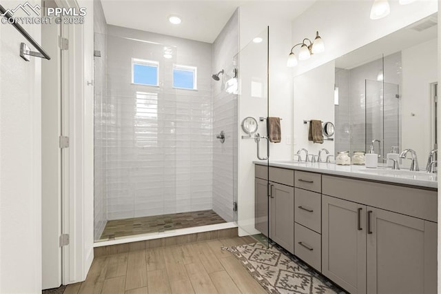 full bathroom featuring a shower stall, wood finished floors, double vanity, and a sink