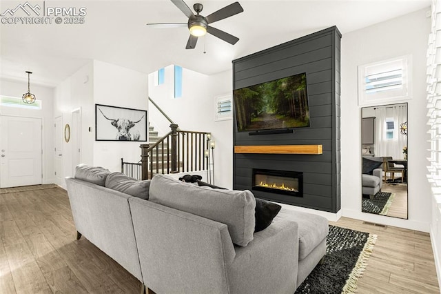 living room with wood finished floors, stairway, a large fireplace, baseboards, and ceiling fan