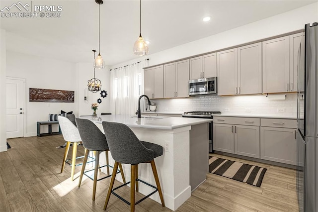 kitchen featuring light wood-type flooring, gray cabinets, a sink, tasteful backsplash, and appliances with stainless steel finishes