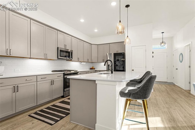 kitchen with a sink, light wood-type flooring, appliances with stainless steel finishes, and gray cabinetry