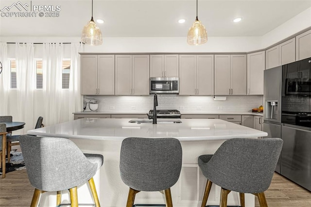 kitchen featuring gray cabinetry, a sink, stainless steel microwave, light countertops, and decorative backsplash