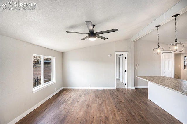 empty room with dark wood finished floors, vaulted ceiling, a textured ceiling, and baseboards