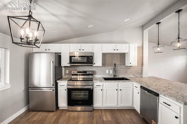 kitchen with lofted ceiling, a sink, appliances with stainless steel finishes, backsplash, and dark wood finished floors