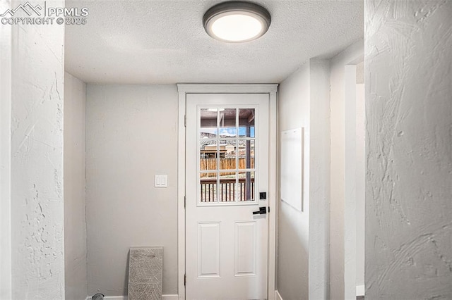 doorway to outside with a textured wall and a textured ceiling