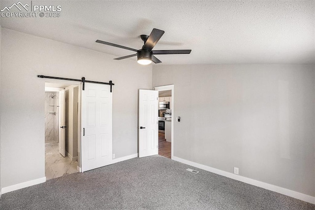 unfurnished bedroom with carpet floors, lofted ceiling, visible vents, a barn door, and baseboards