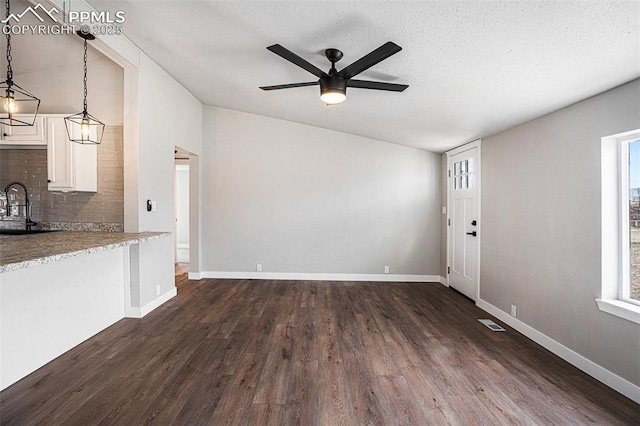 unfurnished living room with vaulted ceiling, dark wood-type flooring, plenty of natural light, and a sink