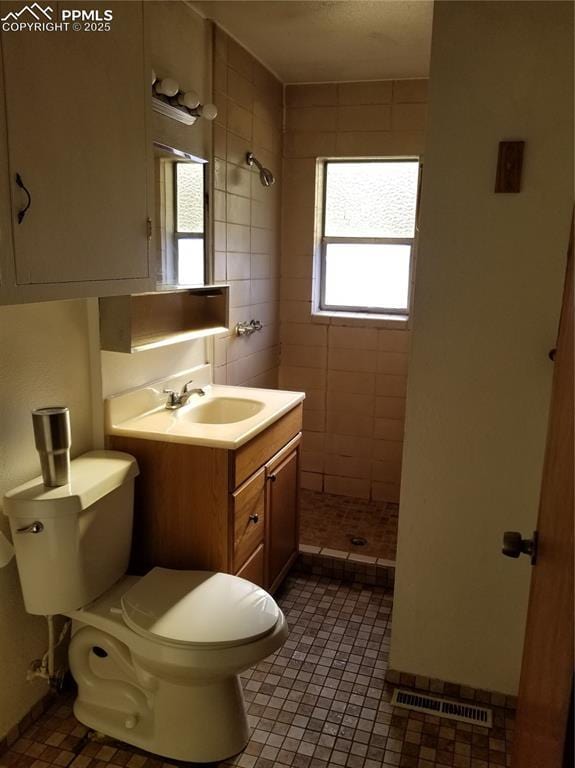 bathroom featuring visible vents, a tile shower, vanity, and toilet