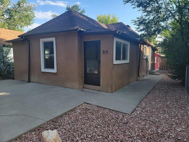 exterior space featuring a patio area, roof with shingles, fence, and stucco siding