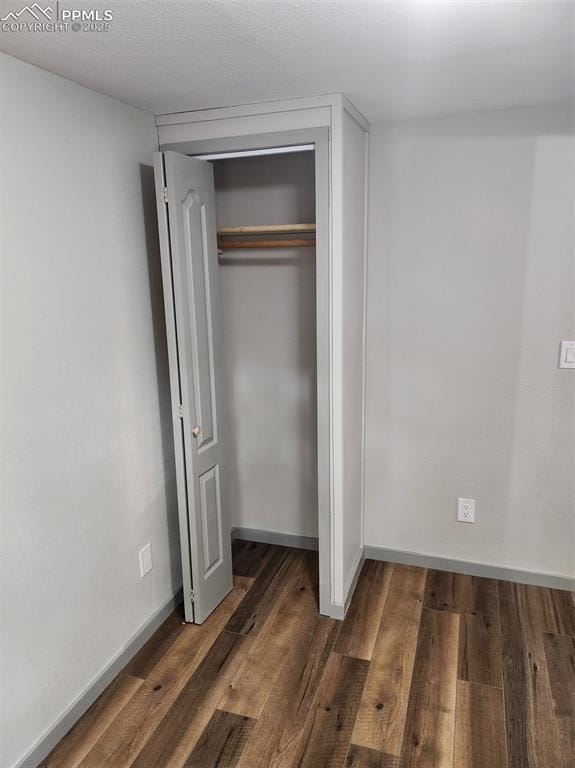 unfurnished bedroom featuring wood-type flooring, a textured ceiling, baseboards, and a closet