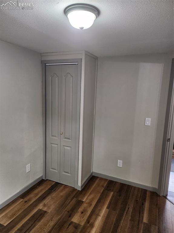 unfurnished bedroom with a closet, dark wood finished floors, a textured ceiling, and baseboards