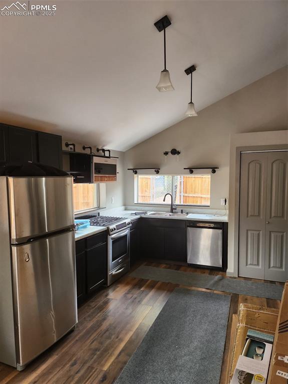 kitchen with stainless steel appliances, light countertops, dark cabinetry, and vaulted ceiling