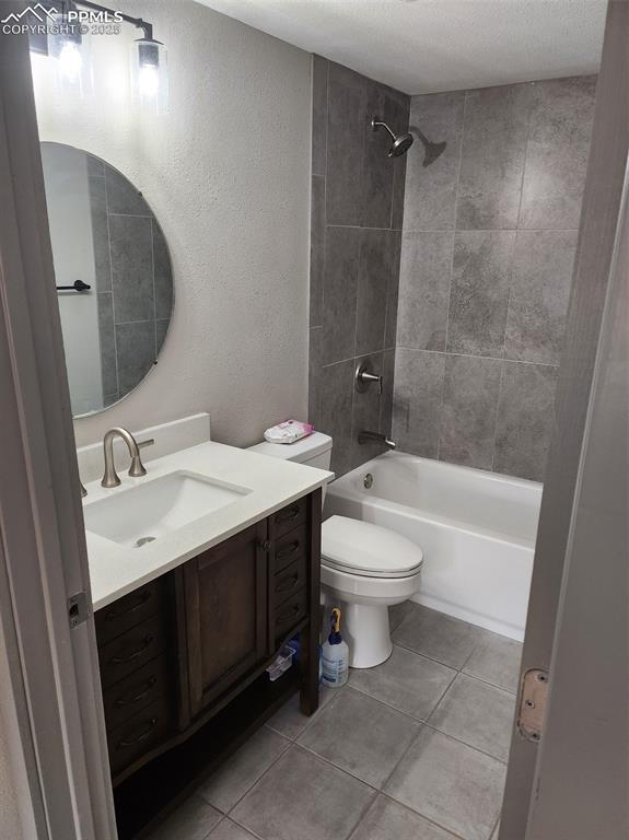 full bath featuring toilet, vanity, a textured ceiling,  shower combination, and tile patterned flooring