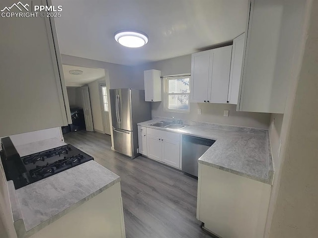 kitchen with wood finished floors, a sink, white cabinetry, light countertops, and appliances with stainless steel finishes