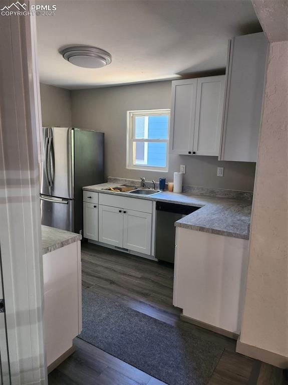 kitchen with stainless steel appliances, a sink, white cabinetry, light countertops, and dark wood finished floors