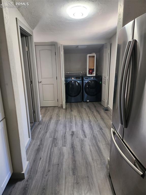 clothes washing area featuring laundry area, a textured ceiling, separate washer and dryer, and wood finished floors