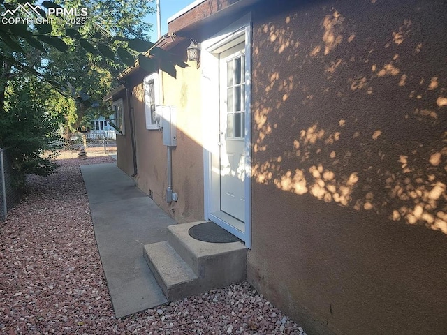 view of property exterior featuring entry steps, fence, and stucco siding