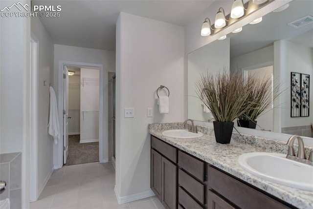 full bath with a spacious closet, double vanity, a sink, and visible vents