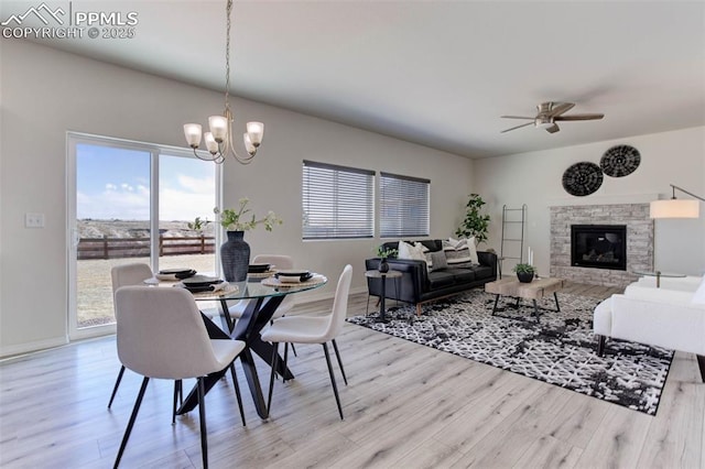 dining room featuring ceiling fan with notable chandelier, a fireplace, baseboards, and wood finished floors