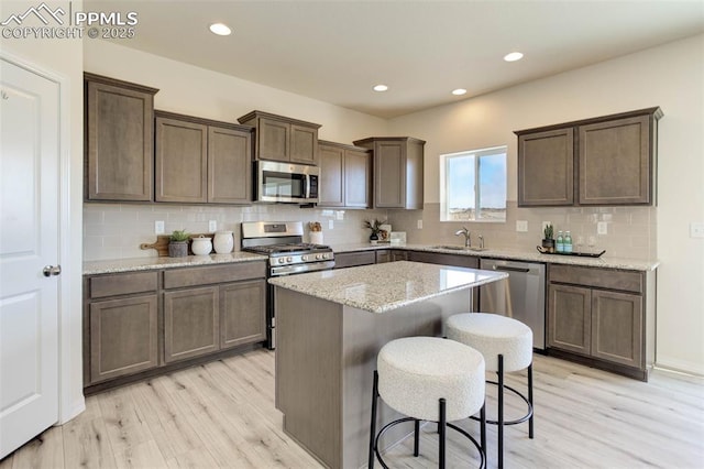 kitchen with light wood finished floors, a breakfast bar area, appliances with stainless steel finishes, and a sink