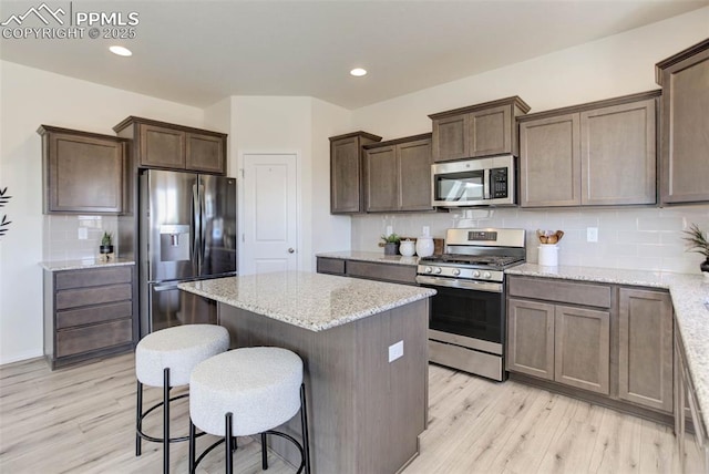 kitchen featuring light stone counters, a center island, backsplash, appliances with stainless steel finishes, and light wood-type flooring