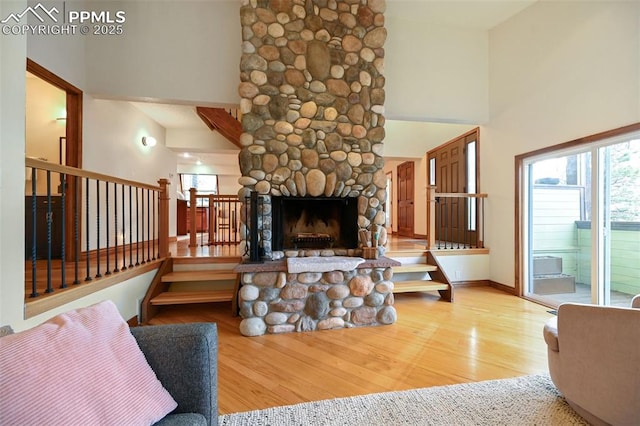 living area with a stone fireplace, a towering ceiling, and wood finished floors