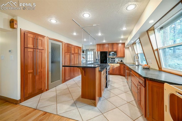 kitchen with a textured ceiling, a breakfast bar area, stainless steel appliances, brown cabinets, and a center island