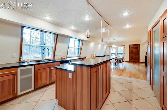 kitchen featuring light tile patterned floors, dark countertops, a sink, and a center island