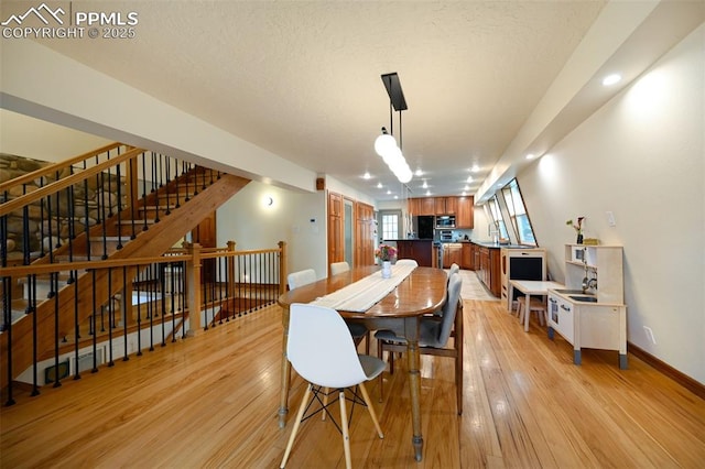 dining area featuring light wood-style floors, a textured ceiling, and baseboards