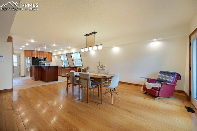 dining area featuring rail lighting, visible vents, light wood-style floors, a textured ceiling, and baseboards