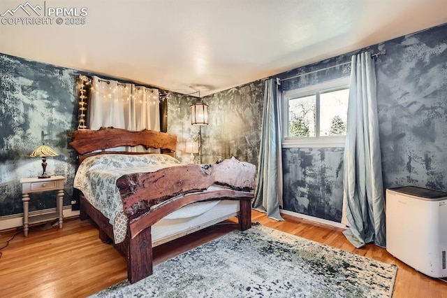 bedroom with a baseboard heating unit, wood finished floors, and baseboards